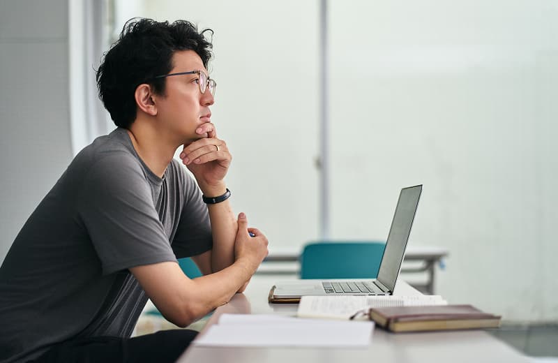 デスクで頬杖をついて考えている男性の写真
