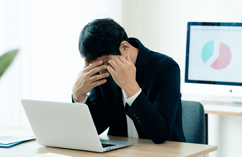 パソコンの前で頭を抱えている男性の写真