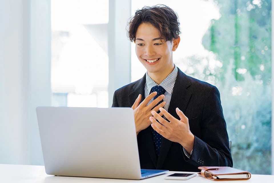 ノートパソコンの前でスマートフォンを操作している男性の写真