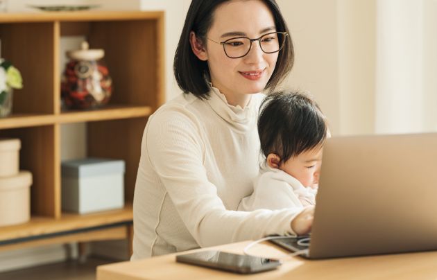 赤ちゃんを抱いてリモートワークをする女性の写真